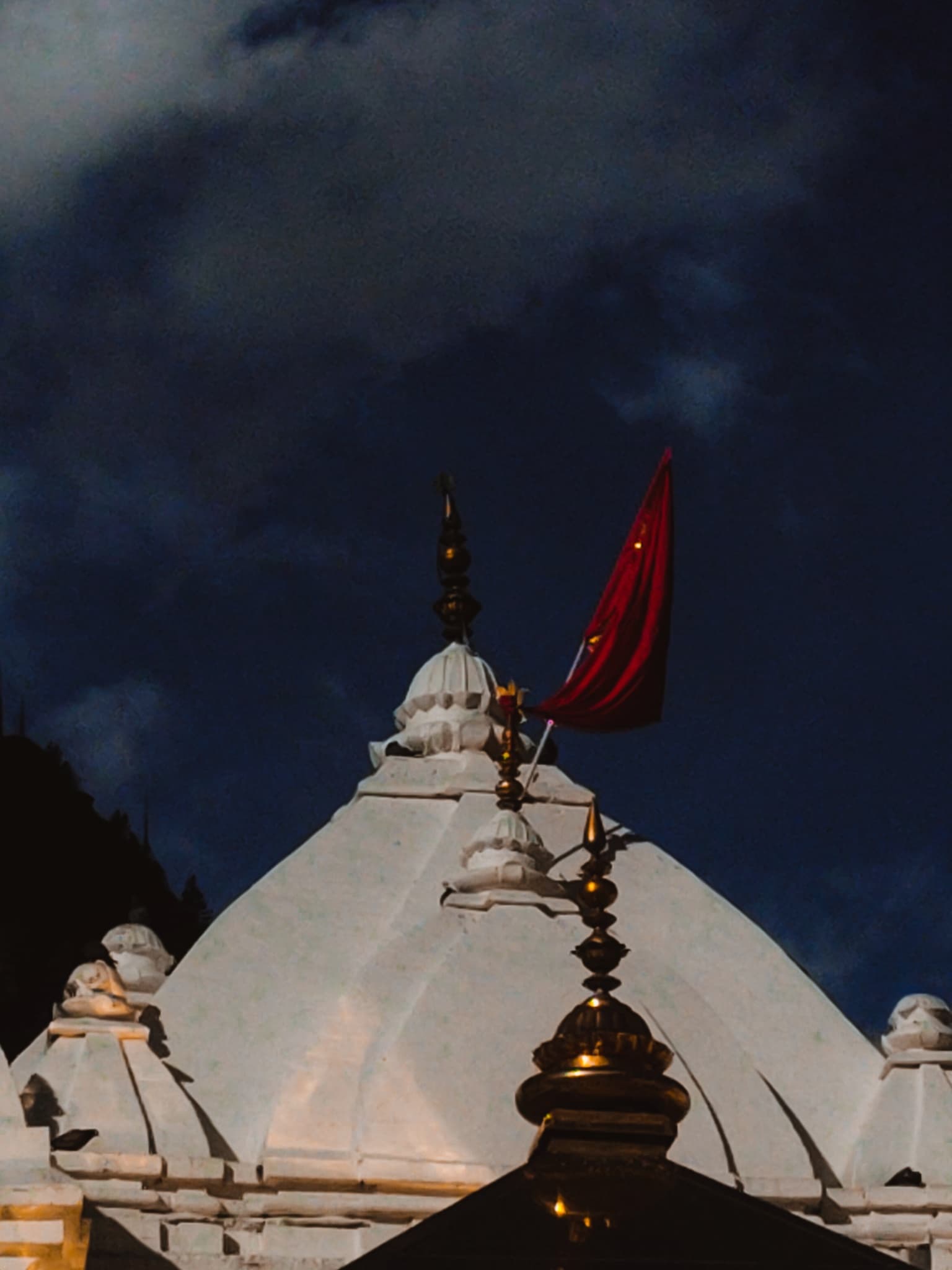 White marble temple shikhara with a saffron flag flying against a deep blue night sky