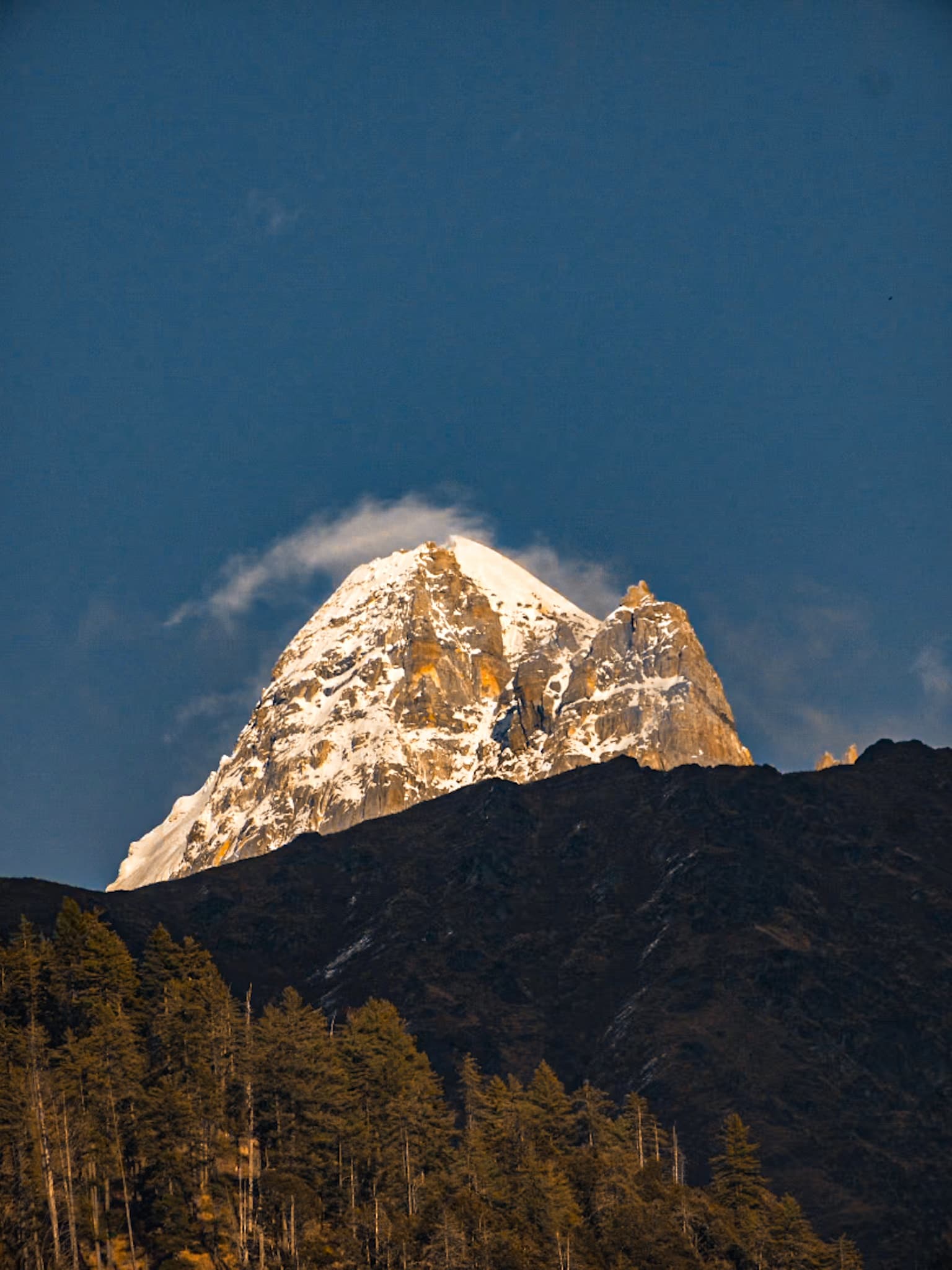 A pyramidal snow-covered Himalayan peak glowing in golden alpenglow at dusk